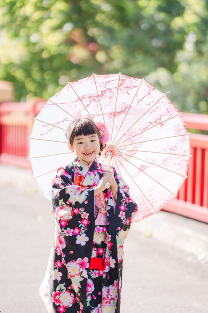 札幌護国神社の赤い橋で和傘を持って微笑む七五三の女の子