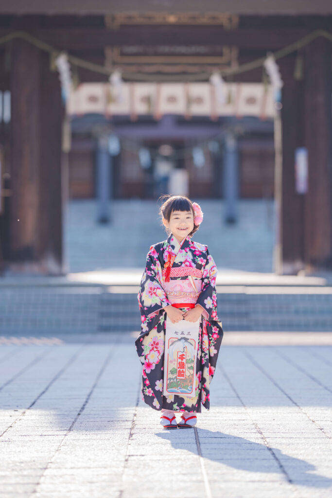 札幌護国神社を背景に千歳飴を持って立つ着物姿の七五三の女の子