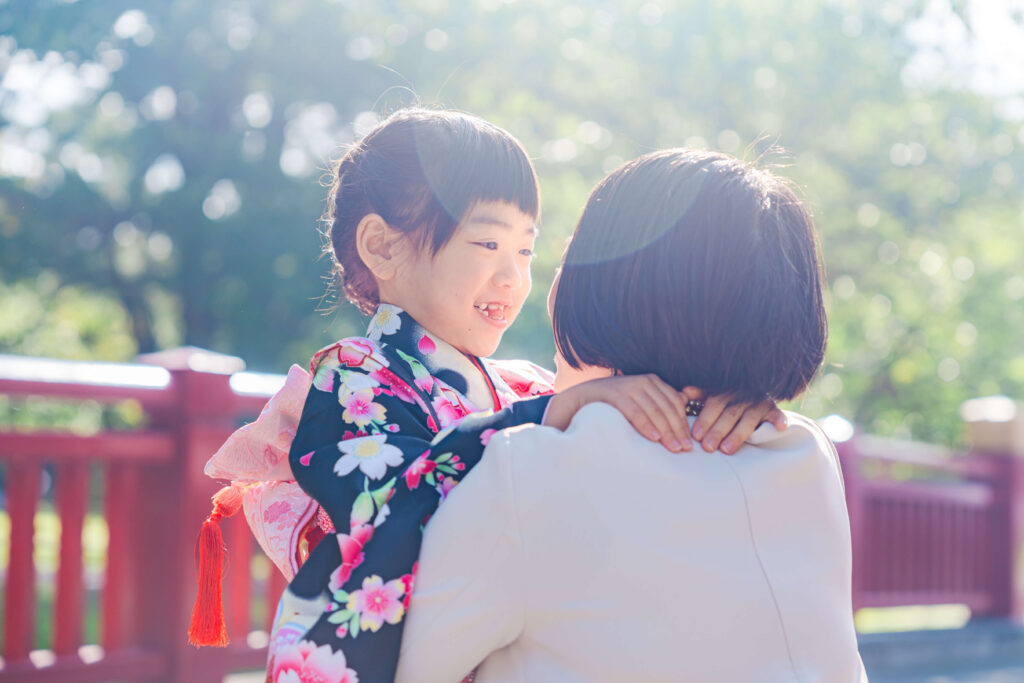 札幌護国神社の赤い橋を背景にお母さんに抱っこされて笑う七五三の女の子